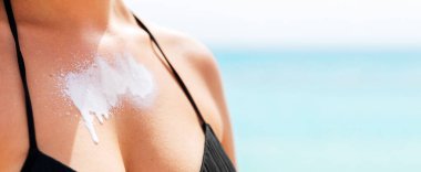 Güzel genç bir kadın plajda güneş kremiyle gün ışığının tadını çıkarıyor..