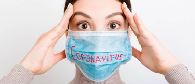 Beyaz arka planda Coronavirus yazılı tıbbi maske takan oldukça şok olmuş bir kadının portresi. Coronavirus konsepti. Solunum koruması.