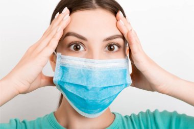 Beyaz arka planda tıbbi maske takan şok olmuş genç bir kadının portresi. Sağlığınızı koruyun. Coronavirus konsepti.