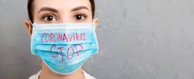Tıbbi maskeli bir kadının portresi Coronavirus yazısını gri çimento arka planda durdurmuş. Coronavirus konsepti. Solunum koruması.