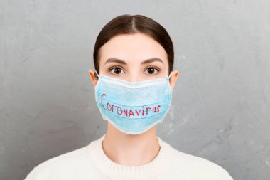 Gri çimento arka planında Coronavirus metni olan tıbbi maskeli bir kadının portresi. Coronavirus konsepti. Solunum koruması.