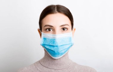 Beyaz arka planda tıbbi maske takan genç bir kadının portresi. Sağlığınızı koruyun. Coronavirus konsepti.
