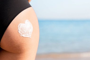 Deniz arka plan üzerinde bir kadın kalça güneş kremi yapılmış kalp şekli.