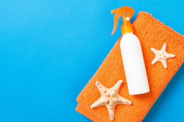 Summer beach flat lay accessories. Sunscreen bottle cream, towel and seashells on colored Background. Travel holiday concept with copy space.