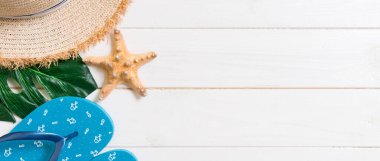 Hasır şapka, yeşil yaprak, mavi parmak arası terlik ve beyaz ahşap arka planda deniz yıldızı. Fotokopi alanı ile yaz tatili konsepti.
