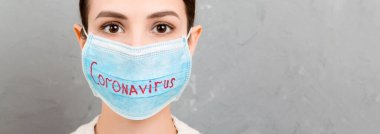 Gri çimento arka planında Coronavirus metni olan maske takmış üzgün bir kadının portresi. Coronavirus konsepti. Solunum koruması.
