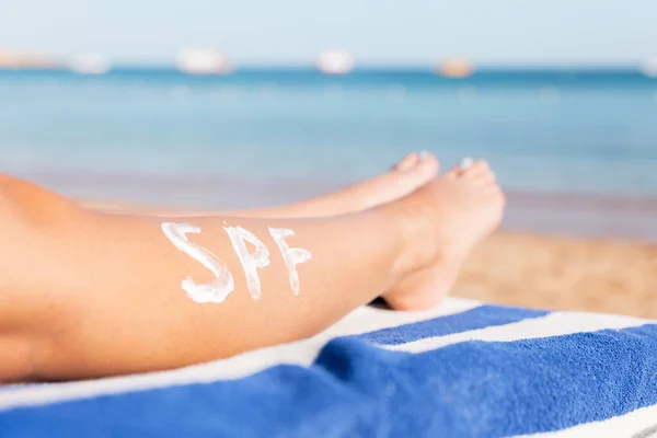 Female legs with spf word made of sun cream at the beach. Sun protection factor concept.