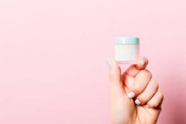 Pembe arka planda kadın eli kozmetik kavanozu ve tasarımınız için boş bir alan..