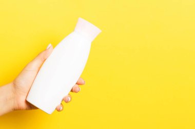 Kozmetik şişesini kadın eliyle kapatın. Sarı arka planda fotokopi alanı ile birlikte..