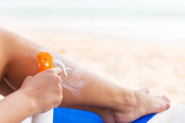 女孩正在海滩用喷雾把防晒霜涂在腿上 — 图库照片