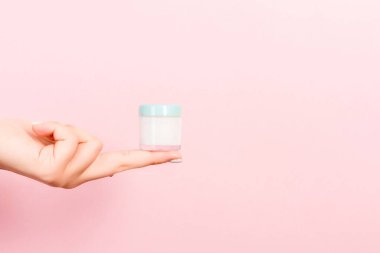 Pembe arkaplandaki kozmetik kavanozunun fotokopi alanı olan kadın elini kapat.