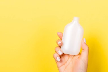 Kozmetik şişesini kadın eliyle kapatın. Sarı arka planda fotokopi alanı ile birlikte..