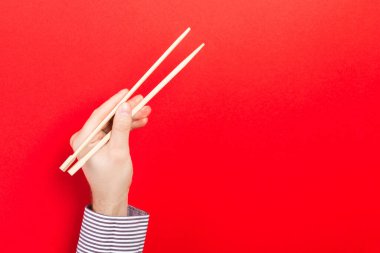 Kırmızı arka planda yemek çubukları olan bir erkek. Tasarımınız için emty alanı olan geleneksel Asya yemekleri.