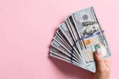Renkli arka planda yüz dolar bir fan tutan kadın el üst görünümü. Kredi konsepti. Kopyalama alanı ile Refah kavramı.