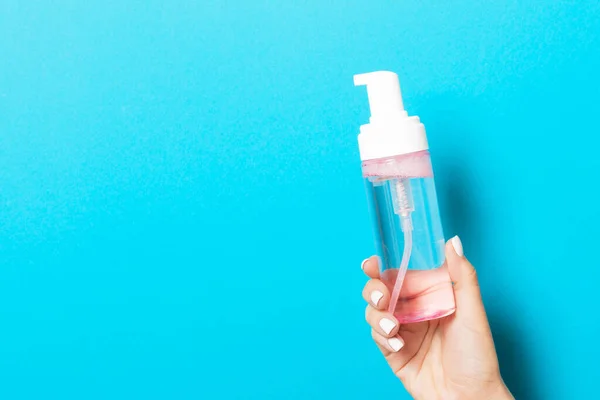 A spray of cosmetic product in a female hand at blue background with copy space.