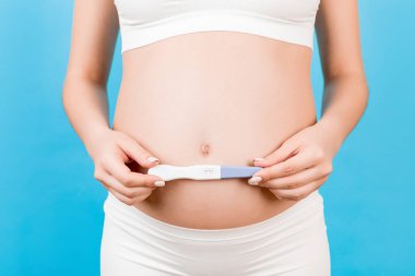 Beyaz iç çamaşırlı hamile bir kadının mavi arka planda karnına yapılan pozitif hamilelik testini gösteriyor. Çocuk doğurmak üzere. Boşluğu kopyala.