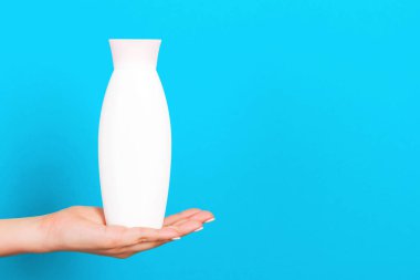 Kozmetik şişesini kadın eliyle kapatın. Mavi arka planda fotokopi alanı ile birlikte..