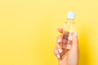 Kadın eli, tasarımınız için boş olan sarı arka planda kozmetik şişesini tutuyor..