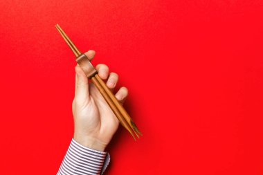 Kırmızı arka planda yemek çubuğu tutan erkek eli görüntüsü. Kopya alanı olan Asya yemekleri konsepti.