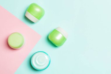 Pembe arka planda kozmetik kaplar, spreyler, kavanoz ve şişeler üst görünümü. Tasarımınız için boş alana sahip yakın çekim görünümü.