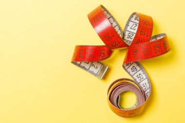 Ölçüm bandının üst görünümü kopyalama alanı olan bir spiral içine küçültülmüş. Sarı arka planda aksesuar ya da sağlıklı beslenme kavramı.