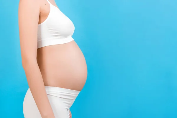 青い背景に妊娠中の女性の腹部のトリミングされた画像 将来の母親は白い下着を着ている 親の概念 スペースのコピー — ストック写真