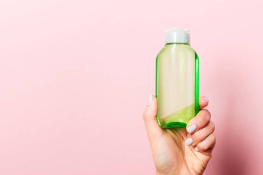 Elinde fotokopi alanı olan kozmetik bir şişeyle pembe arka plan..