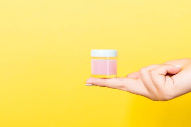 Kadın eli kozmetik kavanozu ve tasarımınız için kopyalama alanı olan sarı arkaplan.