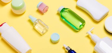 Sarı arka planda farklı ölçekli Kozmetik Kavanozlar ve şişeler bileşimi. Kopya alanı ile güzellik bakımı konsepti.