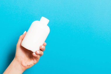 Mavi arka plan, kadın eli kozmetik şişesi ve tasarımınız için kopya alanı..