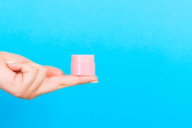 Mavi arkaplanda kadın eli kozmetik kavanozu ve tasarımınız için boş alan.