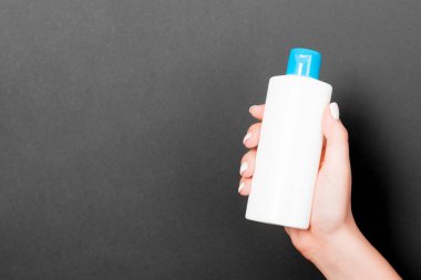 Kadın eli siyah arka planda kozmetik şişesini tutuyor ve tasarımınız için boş bir alan var..