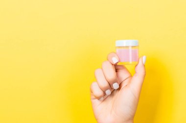 Sarı arka plan, elinde fotokopi alanı olan bir kozmetik kavanozu tutan kadın eli..