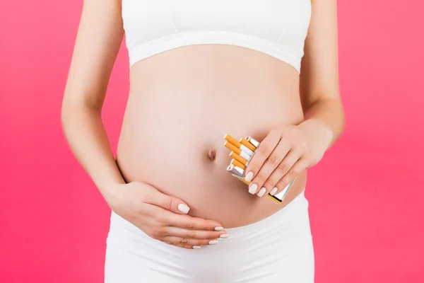 ピンクの背景にタバコのパックを保持白い下着の妊婦のクローズアップ 妊娠中の不健康なライフスタイル 喫煙中毒 — ストック写真