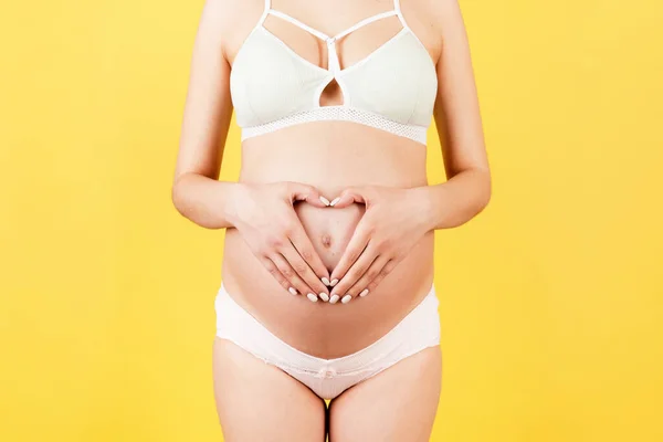 剪下的孕妇形象 穿着五颜六色的内裤 双手放在腹部的黄色背景下做成心脏形状 婴儿碰撞的概念 复制空间 — 图库照片