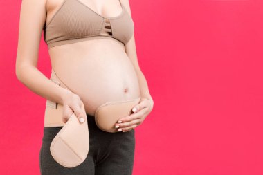 Pembe arka planda, karnına sargı bezi yapıştıran hamile bir kadının fotokopi odası. Ortopedik abdominal destek kemeri kavramı.