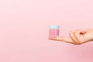 Bir kavanoz kozmetik ürünü pembe arka planda bir kadın elinde fotokopi alanı ile.
