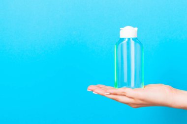 Mavi arka plan, kadın eli kozmetik şişesi ve tasarımınız için kopya alanı..