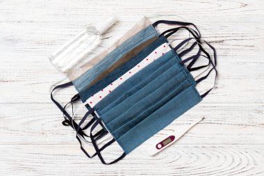 Ev yapımı pamuk maskeler, dijital termometre ve ahşap arka planda alkol el dezenfektanı. Fotokopi alanı ile sağlık hizmeti kavramı.