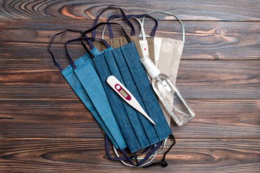 El yapımı pamuk maskesi, alkol el dezenfektanı ve ahşap arka planda fotokopi alanı olan dijital termometre. Koruyucu tıbbi ekipman kavramı.