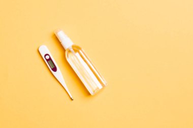 Alkol el dezenfektanı ve dijital termometrenin turuncu arka planda fotokopi alanı ile üst görüntüsü. Koruyucu tıbbi ekipman kavramı.