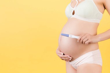 Renkli iç çamaşırlı hamile bir kadının görüntüsü. Sarı arka planda karnına pozitif hamilelik testi yapılmış. Çocuk doğurmak üzere. Boşluğu kopyala.