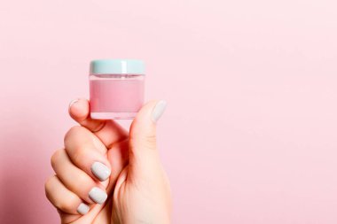 Kozmetik kavanozunu kadın elinde, pembe arka planda fotokopi alanı ile kapat.