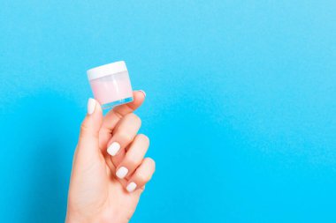 Bir kavanoz kozmetik ürünü mavi arka planda bir kadın elinde fotokopi alanı ile.