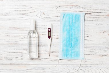 Hijyenik cerrahi maske, dijital termometre ve ahşap arka planda alkol jeli dezenfektanı. Kopya alanı ile koruyucu ekipman kavramı.