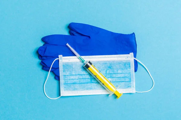 Top view of disposable surgical mask, pair of latex medical gloves and syringe on blue background. Virus protection concept with copy space.