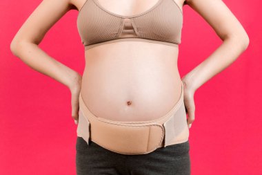 Pembe arka planda sırt ağrısına karşı destekleyici bandajı olan hamile kadının fotokopi odası olan fotoğrafını çek. Ortopedik abdominal destek kemeri kavramı.