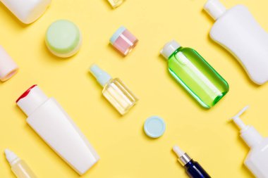 Sarı arka planda farklı kozmetik şişeleri ve kozmetik ürünleri konteynırlarının üst görüntüsü. Kopya alanı olan düz konum.