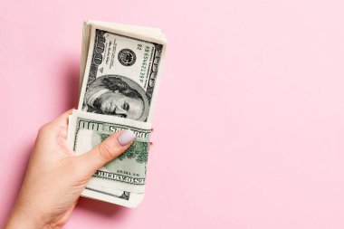 Renkli arka planda yüz dolarlık banknotlar bir paket tutan kadın el üst görünümü. Tasarım için boş alan ile ücret ve maaş kavramı.