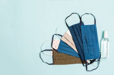 Kişisel korumanın en üst noktası, mavi arka planda bir yığın ev yapımı tekstil maskesi ve alkol el dezenfektanı. Fotokopi alanı ile sağlık hizmeti kavramı.